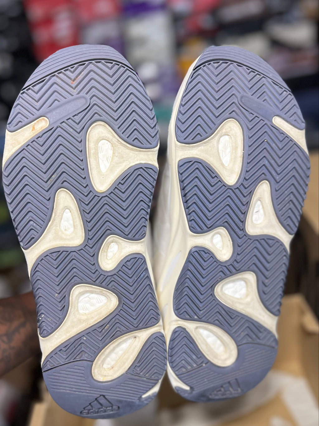 A pair of Adidas Yeezy Boost 380 sneakers shown from the sole, featuring a dusty blue-gray and off-white wavy tread pattern. 