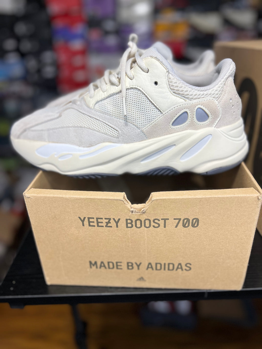 A light gray and white Adidas Yeezy Boost 700 sneaker resting on top of its cardboard box, with the text 'YEEZY BOOST 700' and 'MADE BY ADIDAS' visible on the box.
