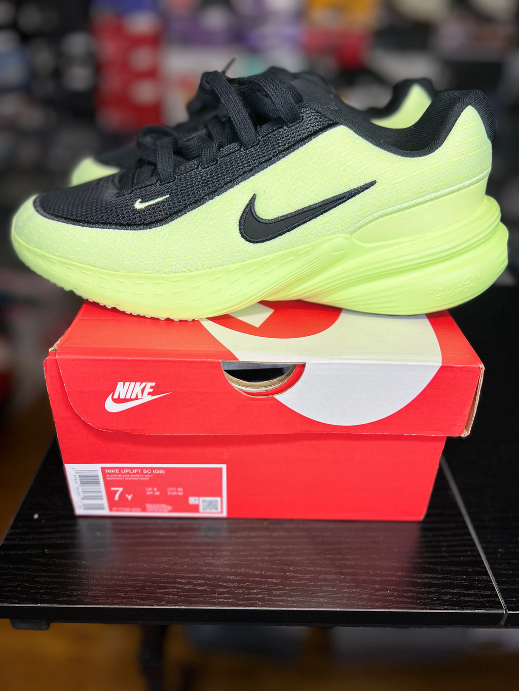 A Nike running shoe in neon yellow-green and black resting on top of its red and white Nike shoebox, placed on a dark wooden table.