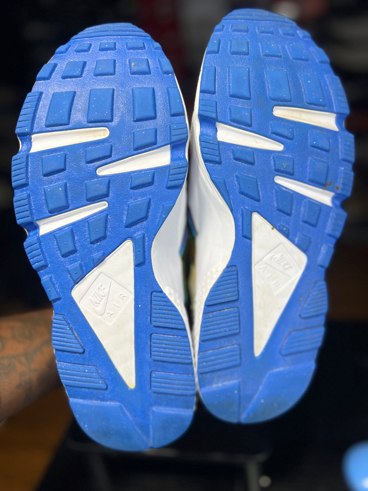 Close-up of the outsoles of a pair of white sneakers with bright blue tread, showing the textured rubber and triangular logo shapes.