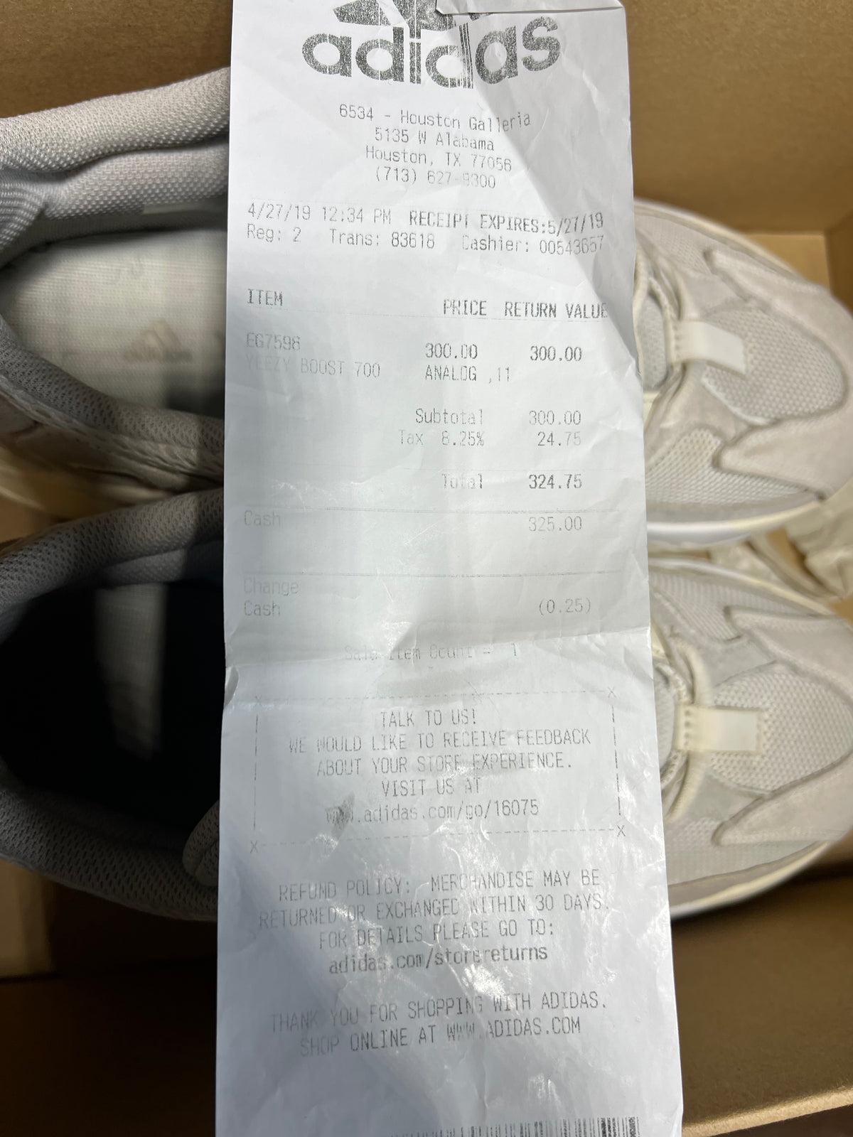 An Adidas receipt paper slip showing a transaction for a pair of sneakers, placed over a pair of off-white Adidas sneakers inside a shoebox.