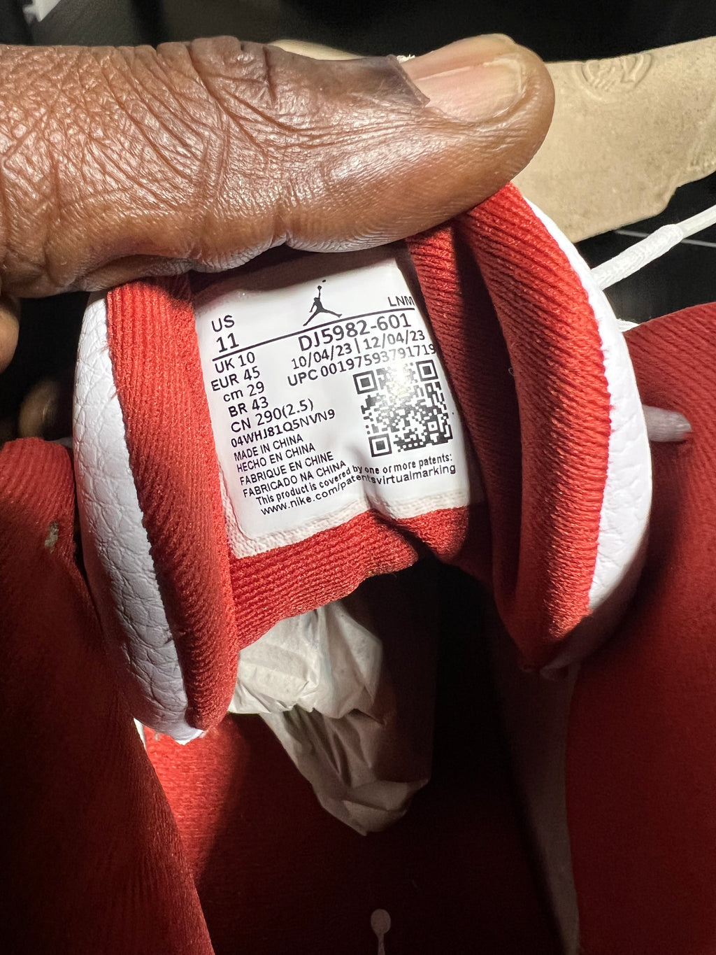Close-up of a red and white Jordan sneaker showing the inner collar and size label, held by a hand. The Jordan logo is visible on the label.